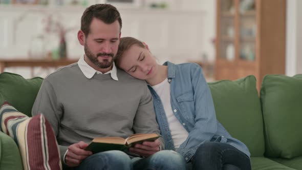 Man Reading Book While Wife Is Sleeping on Sofa