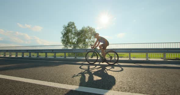 A Sportsman on a Bicycle is Riding Across the Bridge