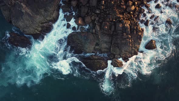 Aerial drone view of ocean blue waves break on high cliff of a rocky mountain at sunrise