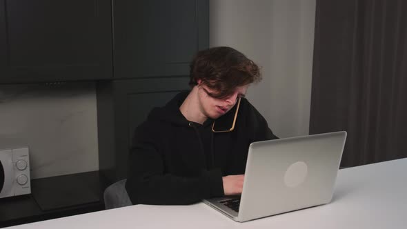 Caucasian Man Talking Phone While Using Laptop at Home Office