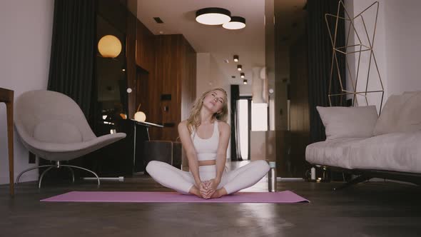 Young Blonde Sitting on a Yoga Mat and Swinging to the Sides