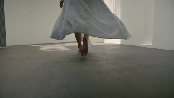 Back View of Woman Wearing a White Dress and Walking a Long White Interior Outdoors