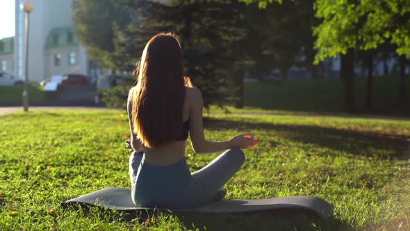 Rear View of Meditative Young Woman Sitting in Lotus Pose and Putting Hands on Knee in Om Position