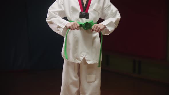 A Little Boy Doing Taekwondo  Tying Up His Green Belt on the Waist