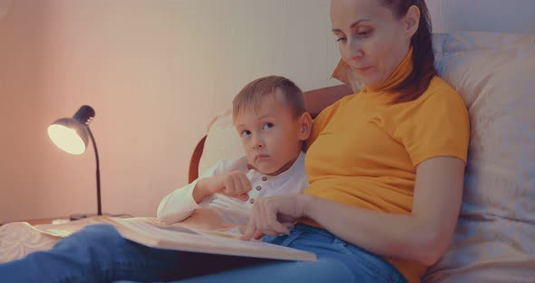 Cute Toddler Boy Reading Book with Mother Before Going to Sleep