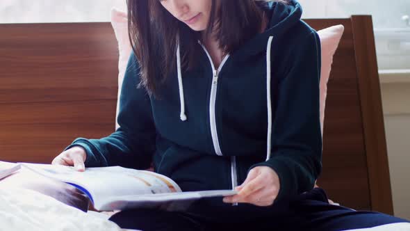 Young woman in hoodie reading magazine 4k