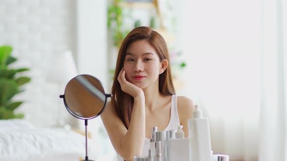 Happy Asian young woman smile and looking in mirror doing skin care touch cheek and beauty treatment