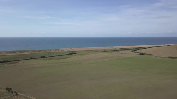 Aerial tracking forward over a vast field on the coat next to Chesil beach. Abbotsbury, Dorset.