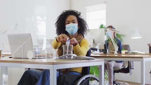 Woman wearing face mask sanitizing her hands at office