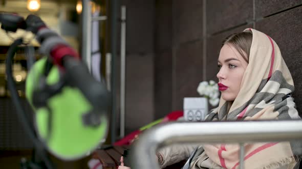 woman drinks coffee from a disposable cup on the veranda of a cafe