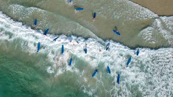 Aerial drone video of a group of surfers on blue boards having fun in the surf