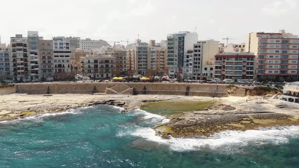 Sliema city seafront with Promenade leading to rocky beach in Malta - Descending aerial shot