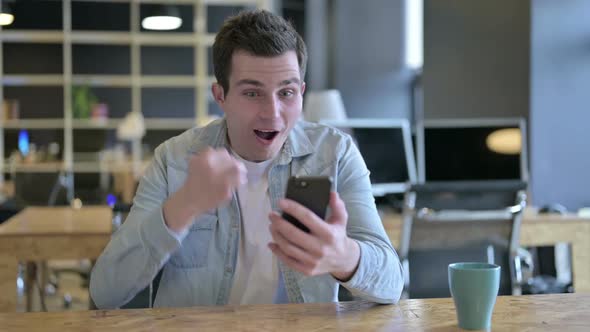 Young Designer Celebrating Success on Smartphone in Modern Office