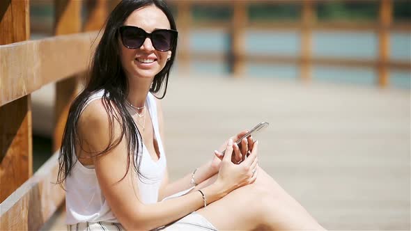 Cute Woman Is Reading Text Message on Mobile Phone While Sitting in the Park.