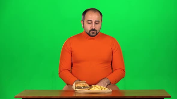 Man with Overweight Looks at Delicious Junk Foods on the Table and Resisting Unhealthy Eating, Green