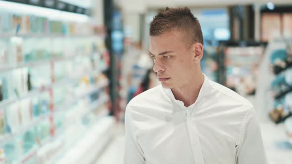 Handsome Purposeful Young Guy in White Shirt Walks Through the Supermarket 