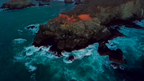 Slow orbit around rocky ocean point deluged by crashing waves at Sand Dollar Beach in Big Sur Califo