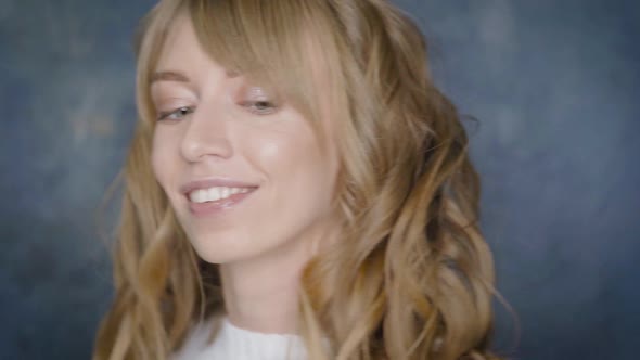 Happy Smiling Girl with Beautiful Blonde Curly Hair Posing in a Beauty Studio.