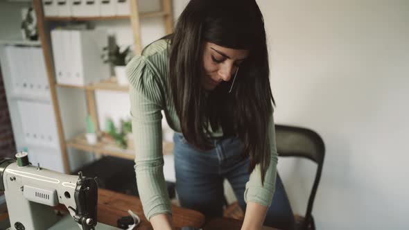 unrecognizable tailor using smartphone and sewing machine in workshop