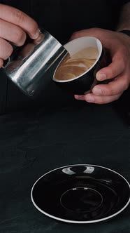 Barista pouring milk in hot coffee and making cappuccino foam in cafe close up, vertical