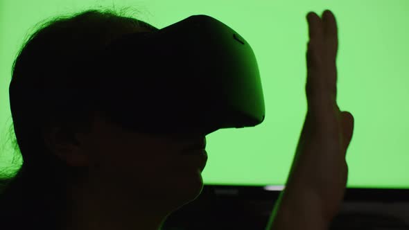 Close-up of a woman's head in VR glasses and her hands making various gestures against a color-chang