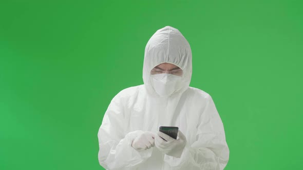 Asian Man Wear Protective Uniform PPE And Use Mobile Phone In The Green Screen Studio