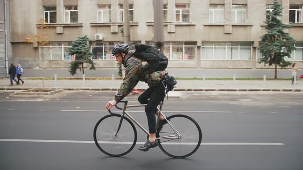 Young Hipster Man in Helmet Riding Fixed Gear Bicycle in the City During Autumn Morning Side View