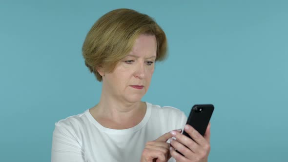 Old Woman Reacting To Loss and Using Smartphone Isolated on Blue Background