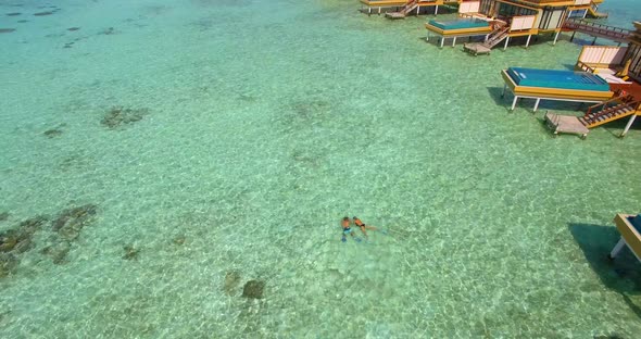 Aerial drone view of a man and woman couple with seascooters snorkeling near overwater bungalows