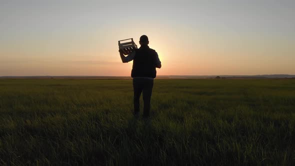 Silhouette Young Farmer Going on the Field at Sunset with Wooden Box with Fresh Vegetables. Healthy