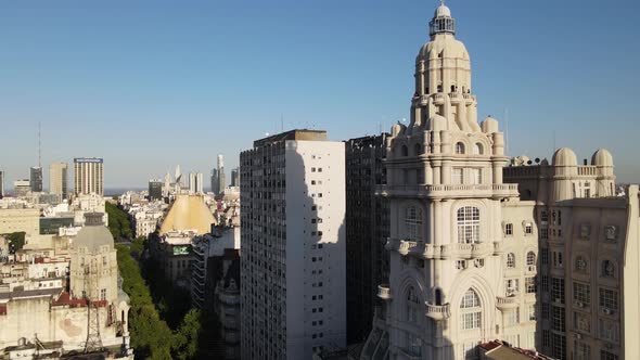 Aerial dolly out of Barolo Palace tower and tree-lined Avenida de Mayo surrounded by Buenos Aires bu