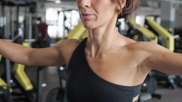 Sporty Woman in Sportswear Spreads Her Hands to the Side with Dumbbells in Gym