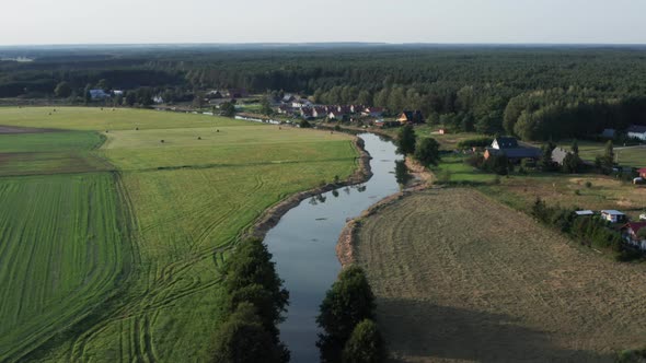 Aerial countryside shot of a curvy river among the fields and farms of a small village by the forest