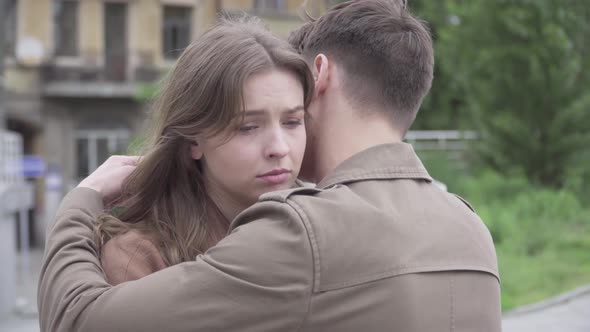 Close-up of Boyfriend Hugging Sad Beautiful Girlfriend on City Street. Upset Caucasian Woman Putting