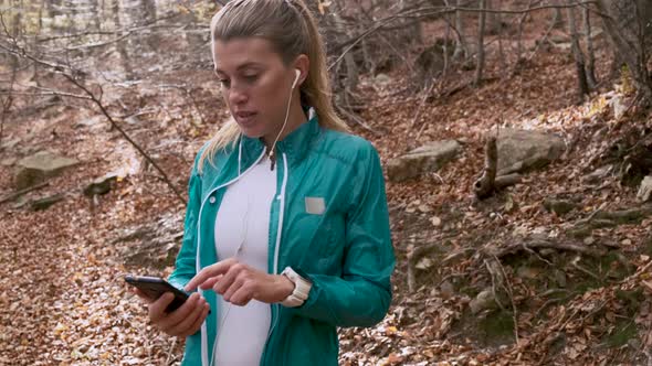 Female jogger with earbuds using smartphone in forest