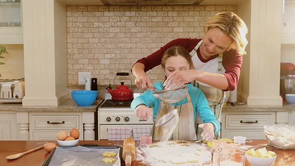 Smiling mother and daughter wearing apron sieving flour together 4K 4k