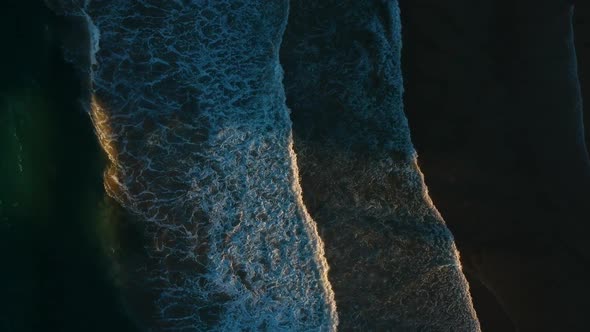 Waves breaking on a dark beach with the sunlight breaking through