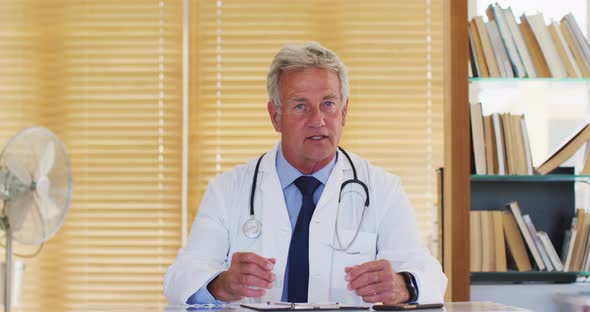 Portrait of male caucasian doctor of talking looking at camera while sitting in hospital