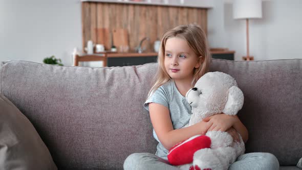 Smiling Cute Baby Girl Relaxing on Comfortable Couch Hugging Teddy Bear Feeling Love Friendship