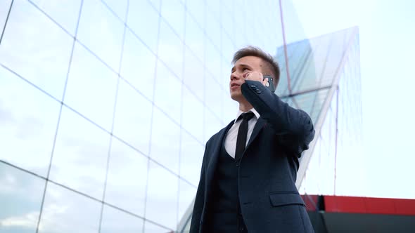 Businessman Talking on Phone Against the Building with a Glass Facade