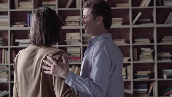 Caucasian Gay Couple Choosing Books To Read on Shelves and Hugging. Back View of Happy Smiling Men