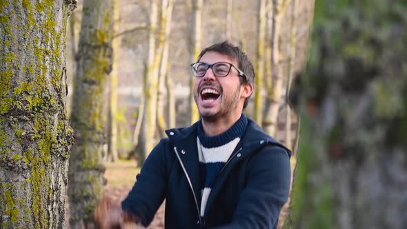 Happy Young Man Smiling and Throwing Leaves with Open Arms, in Autumn Park. 