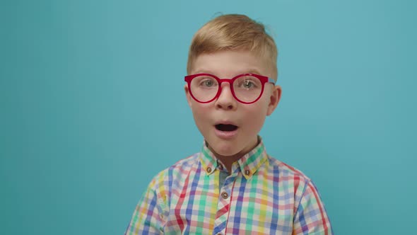 Surprised Kid in Eye Glasses Opening Mouth Standing on Blue Background