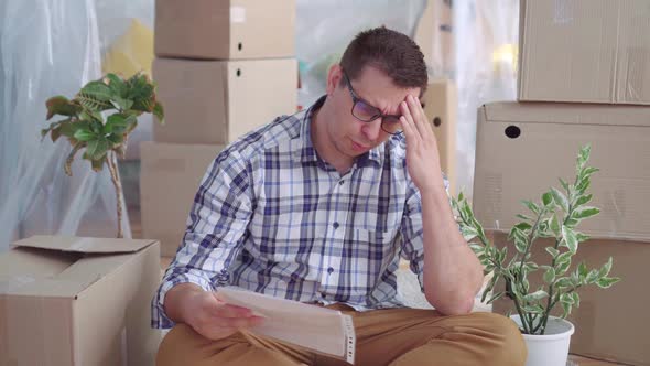 Tired and Upset Middleaged Man with Glasses Among the Boxes To Movereads the Documents for Eviction