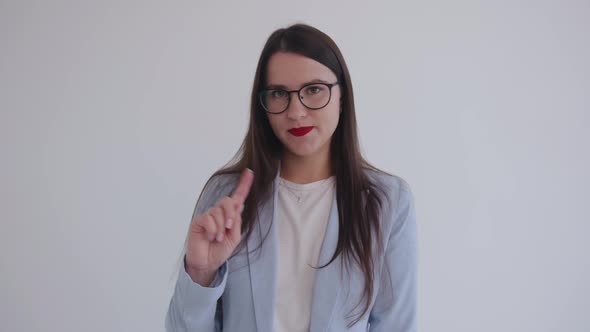 A Confident Young Business Woman Stands on a White Background and Shows with Gestures and Her Head
