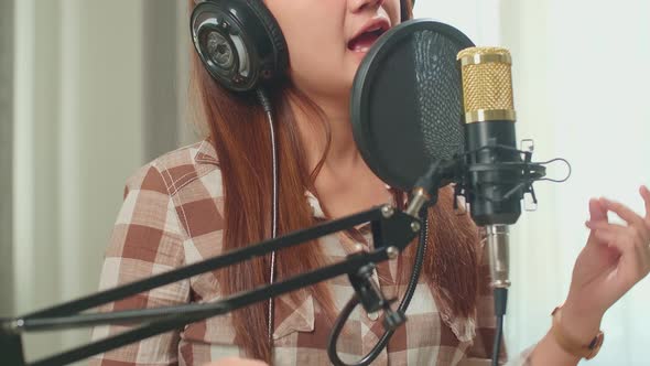 Young Asian Woman In Headphones Singing Into Microphone During Online Livestream In Podcast Studio