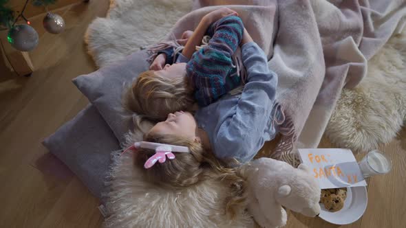 Top View Relaxed Hugging Little Brother and Sister Sleeping at New Year Tree on Christmas Eve with