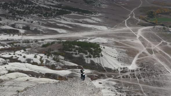 Aerial Panoramic View Active Hiker Couple Hugging on Top of White Rock Surrounded By Hilly Terrain