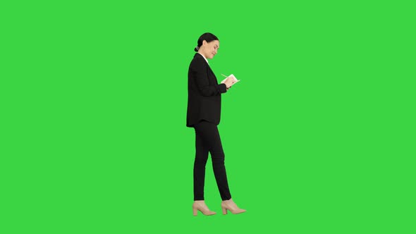 Concentrated Woman in a Suit Writing Business Ideas in Her Notepad While Walking on a Green Screen