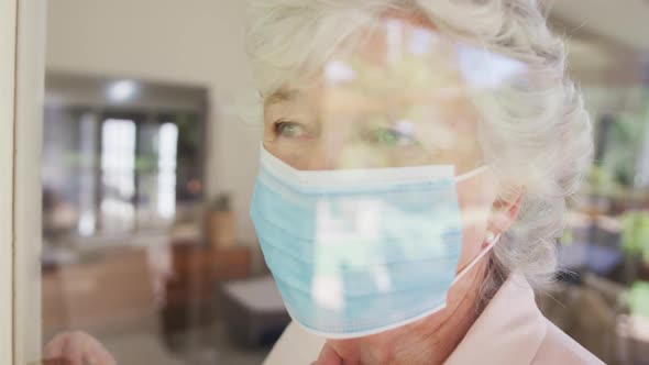 Sad senior caucasian woman wearing face mask seen through window in slow motion